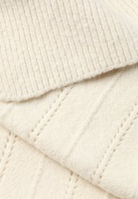 Țesătură tricotată de culoare crem, cu o textură zimțată în partea de sus și o textură modelată în partea de jos, cu linii diagonale.