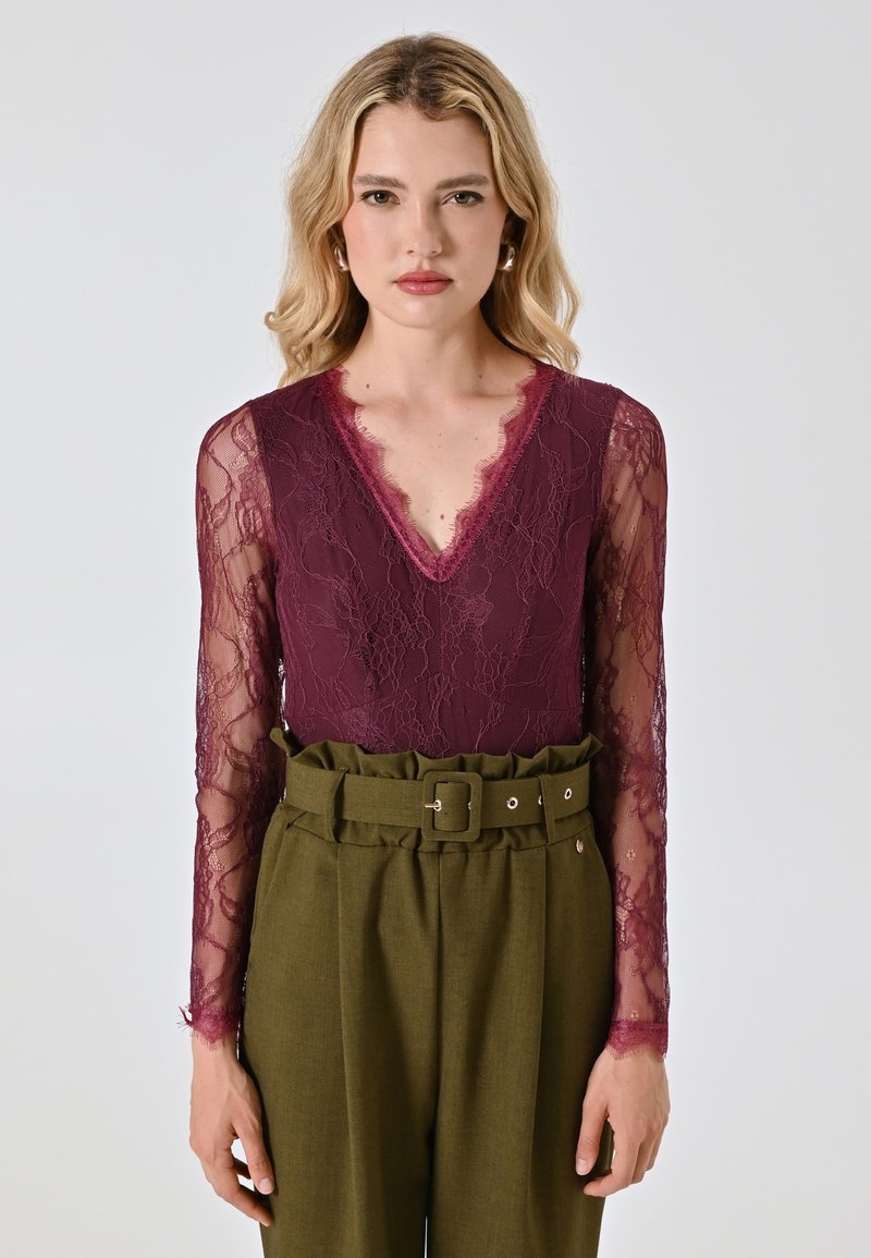 Bordeaux kant bodysuit met v-hals en doorzichtige lange mouwen, gecombineerd met hoog-waist olijfgroene broeken met een ceintuur.
