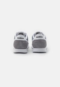 Grå nubuck- og syntetiske joggesko med hvite detaljer, med avrundet tå, polstret såle, og "Reebok"-logo på baksiden av hælen.