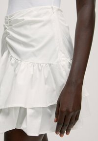 Witte rok met een gerimpelde zoom, gemaakt van lichte stof. Voorzien van een geraffineerde detail bij de taille en een zijrits voor sluiting.
