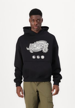 Schwarzer Kapuzenpullover mit einem großen Grafikdesign und dem Text "LOWLIGHTS" sowie runden Aufnähern. Weicher Stoff, lässige Passform, gerippte Bündchen.