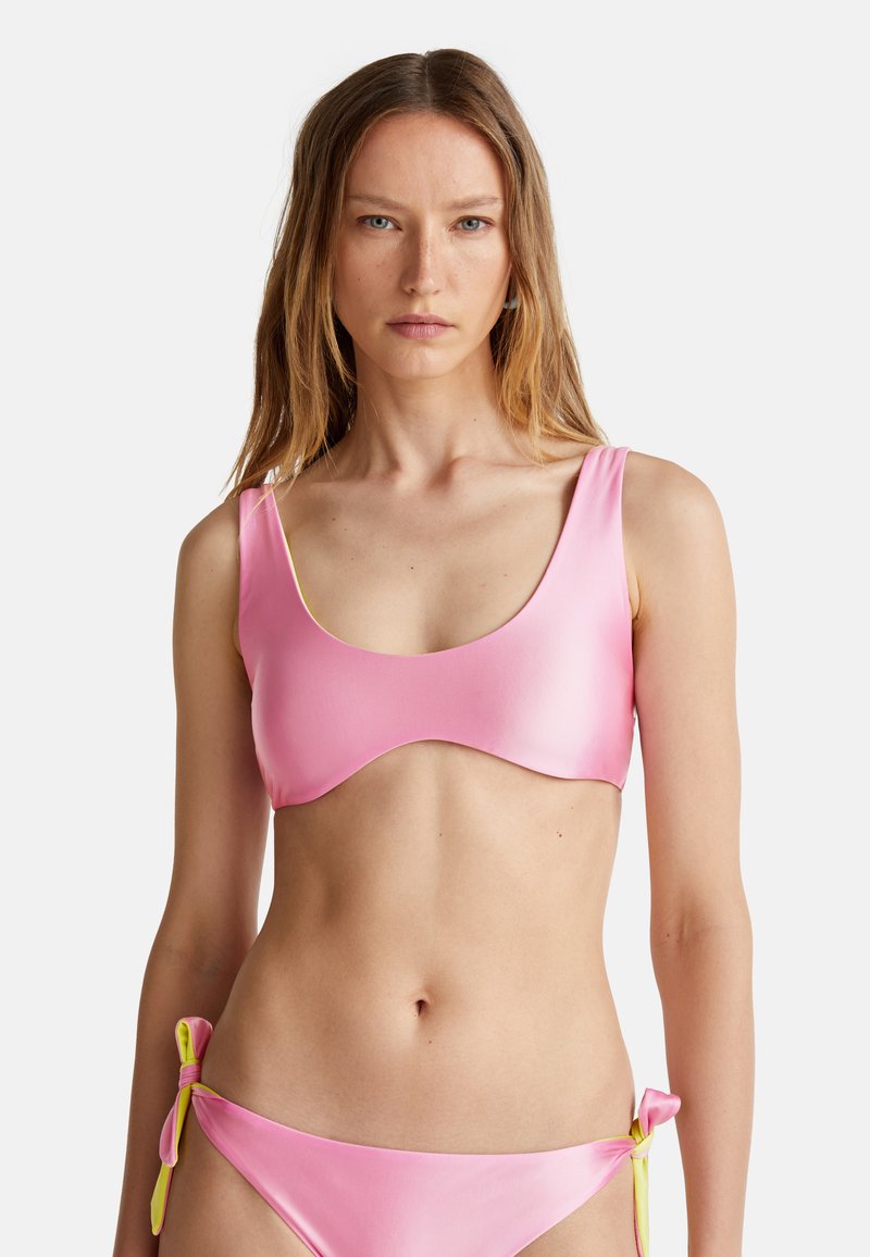 Růžový bikini set s hladkým, lesklým povrchem. Horní část má kulatý výstřih a široká ramínka. Spodní část má boční zavazování s žlutým akcentem.