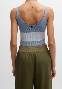 Pletený crop top s V-zadním výstřihem, který má modré a světle modré svislé pruhy. Vybavený s vysokým pasem olivově zelené kalhoty.