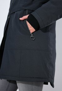 Tmavá, izolační bunda s hladkým povrchem, která má zipovou kapsu a lem spadající pod pas. Barva: antracitově šedá.