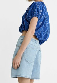 Top corto azul con mangas abullonadas y bordado floral blanco; combinado con pantalones cortos de mezclilla azul claros de cintura alta y bolsillos traseros.