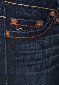 Mörkblå denimjeans med en framficka med kontrasterande orange sömmar, kopparnitar och subtila texturerade linjer.