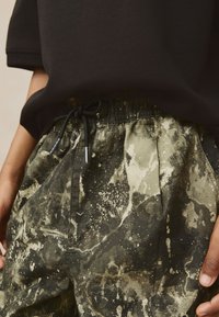 Green and black patterned shorts with a drawstring waist, featuring a textured fabric and splatter design in various shades.