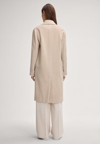 Beige wollen mix jas met een geknipte kraag, lange mouwen en zijzakken, met een rechte snit en subtiele naden aan de achterkant.