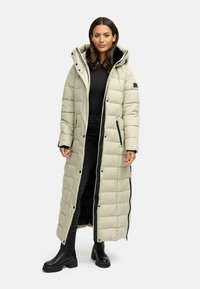 Lang, lys beige pufjakke med hætte, lynlåse og sorte detaljer. Jakken har et quiltet design og går til midt på læggen.