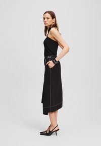 Zwarte geribbelde tanktop gecombineerd met een zwarte rok met witte stikdetails en zijzakken, aangevuld met zwarte puntige hakken.