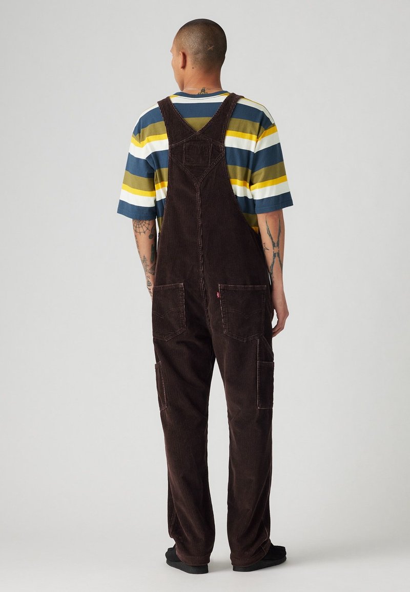 Bruna kordflortoverall med en lös passform, som har två framfickor och justerbara axelremmar, tillsammans med en randig färgblockerande t-shirt.