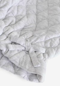 Couverture matelassée en tissu gris clair avec un motif texturé et une fermeture en nœud papillon. Matériau doux avec des variations subtiles de teinte.