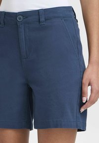 Kék pamut rövidnadrág egyenes szabással, gombos záródással, övtartókkal és ferde oldalsó zsebekkel. Texturált anyag sima felülettel.