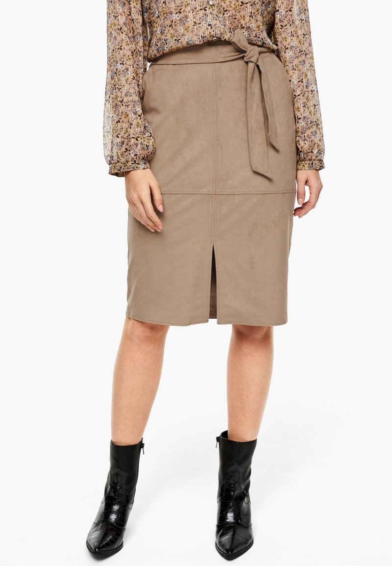 Femme portant une jupe crayon beige longueur genoux avec fente devant et ceinture nouée, un chemisier à manches longues fleuri et des bottines noires à bouts pointus.