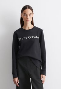Mustmust shirt valge "Marc O’Polo" tekstiga, pikad varrukad, ümmargune kaelus ja pehme tekstuur. Kandunud mustade lõikega pükstega.