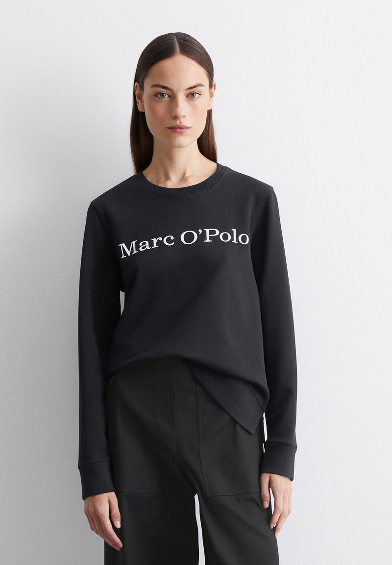 Mustmust shirt valge "Marc O’Polo" tekstiga, pikad varrukad, ümmargune kaelus ja pehme tekstuur. Kandunud mustade lõikega pükstega.