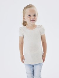 Lys beige kortermet topp med ribbestruktur og blondekant ved halsen, kombinert med tettsittende lyseblå jeans.