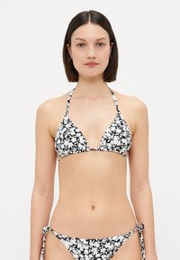 Svart-hvitt blomstermønster bikini med trekantet topp med halterneck-stropper og sidesnøring på bunnene. Glatt stoff med lett tekstur.