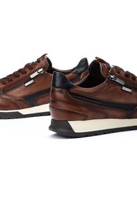 Sneakers in pelle marrone con accenti neri, forma arrotondata, superficie texturizzata e cerniere laterali. Presentano una suola intermedia bianca e una suola in gomma.