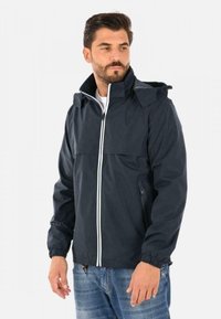 Giacca impermeabile blu navy con colletto alto, chiusura con zip bianca e cappuccio regolabile. Presenta polsini elasticizzati e tasche laterali con zip.