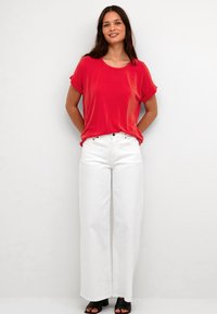 T-shirt rossa a maniche corte con scollatura rotonda abbinata a pantaloni bianchi a gamba larga. Tacchi neri aperti completano l'outfit.