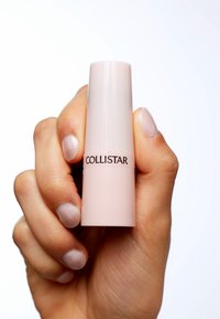 Stick cosmétique Collistar tenu dans une main ; contenant cylindrique, rose clair brillant avec un logo de marque noir à l'avant.