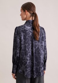 Blusa di un grigio scuro setoso con una sottile stampa leopardata nera. Presenta un colletto a punta, maniche lunghe e polsini con bottoni, silhouette fluida.
