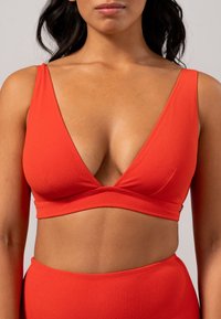 Rode crop top van zachte stof met een diepe V-hals en brede bandjes. Heeft een gewikkeld ontwerp aan de onderkant en subtiele hardware details aan de zijkant.