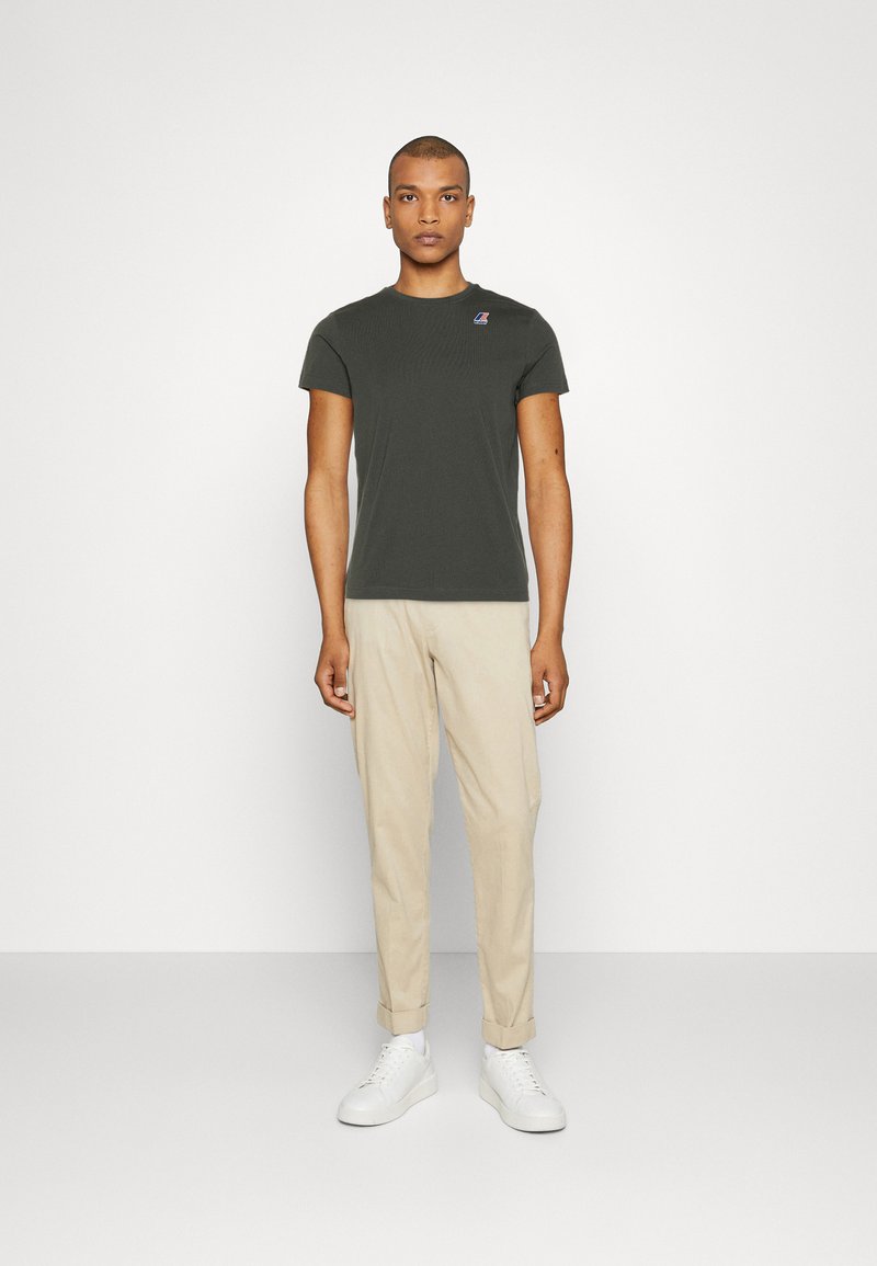 Olijfgroene aangesloten t-shirt met korte mouwen, voorzien van een klein logo op de borst; gecombineerd met lichtbeige chinos en witte sneakers.