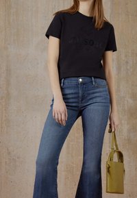 Musta puuvillainen t-paita, jossa on kohokuvioitu "MISSOB Milano" -logo, yhdistetty hyvin istuviin sinisiin levenevän lahkeen farkkuihin. Mukana pieni oliivinvihreä käsilaukku.