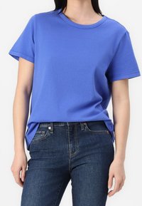 T-shirt en coton bleu à col rond et à manches courtes, associé à un jean en denim bleu foncé. Le t-shirt a une coupe décontractée.