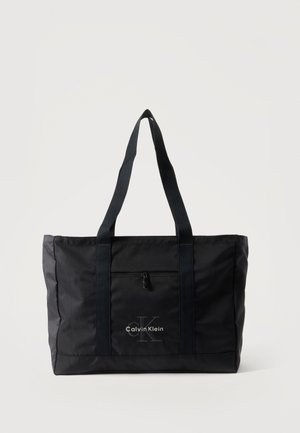 Sac cabas noir Calvin Klein avec deux longues anses, poche zippée à l'avant et logo imprimé au centre devant.