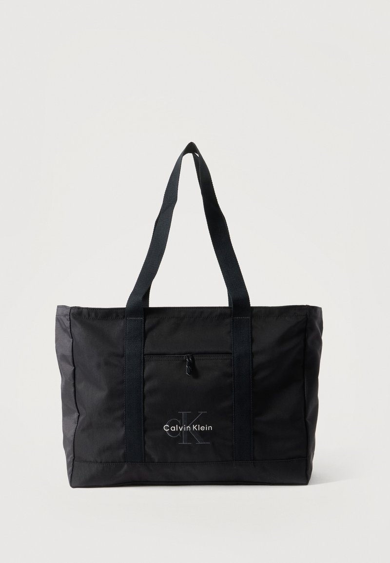 Sac cabas noir Calvin Klein avec deux longues anses, poche zippée à l'avant et logo imprimé au centre devant.