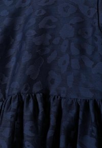 Texturerad mörkblå tyg med subtilt leopardmönster och veckad söm som skapar mjuka plisseringar.