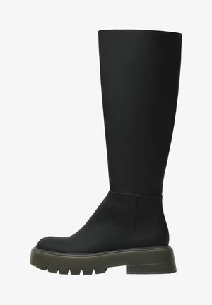 Bottes noires mi-mollet avec une finition mate et lisse, un large tige, un bout rond, et une semelle épaisse texturée de couleur vert foncé contrastante.