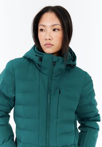 Zelená zateplená zimní bunda s kapucí, s předním zipem, kapsami a logem na hrudi. Hladká textura a mírně lesklý povrch.