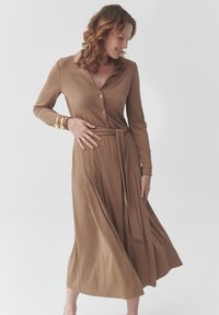 Braunes, langärmliges Kleid mit Kragen, Knopfleiste vorne und einem Bindegürtel in der Taille. Fließender Rock mit Falten, aus weichem Stoff.