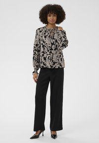 Svart och beige mönstrad blus med lös passform och rynkad halslinje, i kombination med vida svarta byxor och svarta klackar.