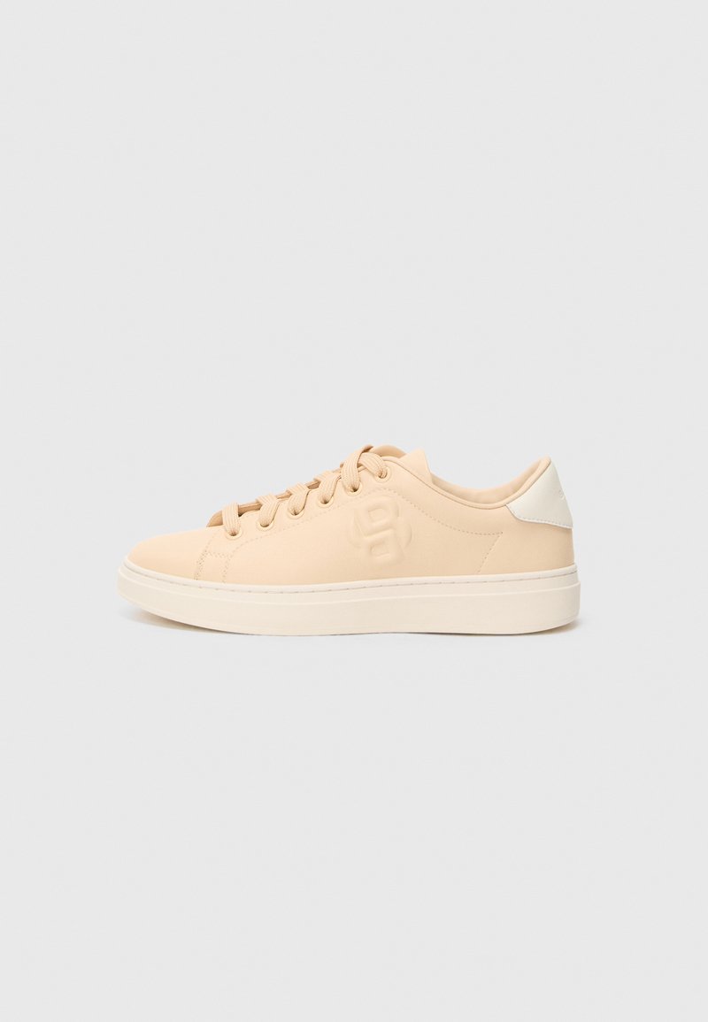 Baskets beige avec une texture lisse et mate, bout arrondi et fermeture à lacets sur le devant. Présente un talon blanc contrastant et un marquage discret sur le côté.