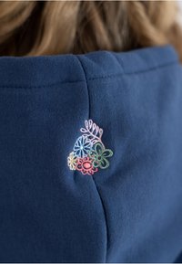 Felpa blu navy con finitura testurizzata e un piccolo motivo floreale colorato ricamato sul retro, vicino alla scollatura.