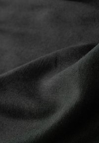 Tissu noir avec une texture lisse, affichant un léger éclat et quelques rides, montrant un motif de tissage uniforme sur la surface.