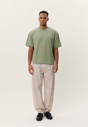 Πράσινο βαμβακερό μπλουζάκι με κοντά μανίκια και τετράγωνη εφαρμογή, συνδυασμένο με μπεζ παντελόνι φαρδιάς γραμμής. Απλός σχεδιασμός, χωρίς ορατά σχέδια ή διακοσμητικά στοιχεία.
