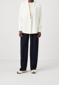 Blazer blanco con un solo botón, combinado con pantalones de pierna ancha en color marino. El conjunto tiene un diseño contemporáneo y ajustado. Textura suave, estilo minimalista.