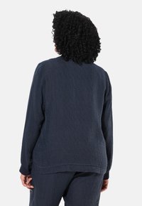 Top a maniche lunghe in tessuto navy con vestibilità rilassata e scollatura rotonda, dotato di polsini a coste, visto da dietro.