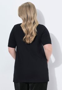 Camisa negra de manga corta con un corte relajado, fabricada en un tejido suave y con aberturas laterales. La vista trasera muestra una textura suave y un diseño simple.