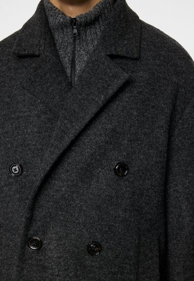 Cappotto doppio petto grigio in lana, con colletto alto, due grandi bottoni neri e una consistenza morbida.
