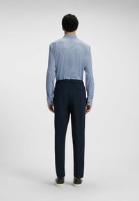Camicia a quadri blu con maniche lunghe, polsini con bottoni e colletto, abbinata a pantaloni e scarpe blu scuro. Tessuto morbido e vestibilità sartoriale.