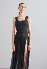 Juodas be rankovių topas, derinamas su permatomu, plisuotu juodu sijonu, turinčiu aukštą iškirpimą. Minimalistinis dizainas su glotnia tekstūra ir elegantiška siluetu.