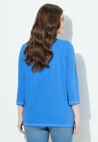 Sininen, pitkähihainen paita, jossa on rento istuvuus. Pehmeä tekstuuri, pyöreä kaula-aukko sekä kontrastiväriset tikkaukset hihoissa ja helmassa.