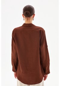 Brown linen shirt with a collar, long sleeves, and buttoned cuffs. The back features a single yoke and a slightly curved hem.